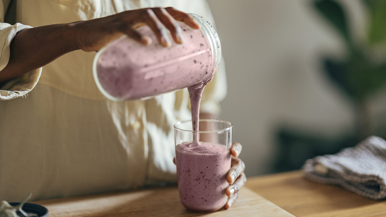 woman pouring a berry smoothie into a glass