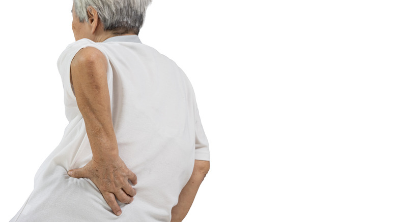 Older man with scoliosis, places hand on waist