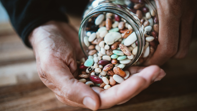 man's hand pouring dried beans out of glass jar