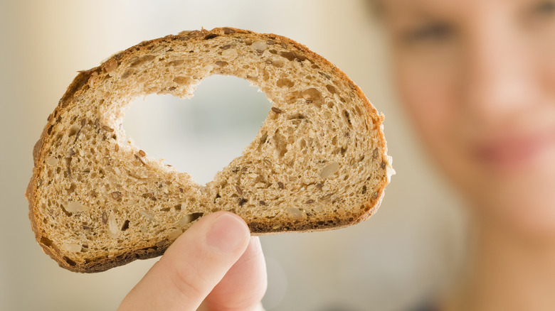 woman holding bread slice with heart cut out in middle