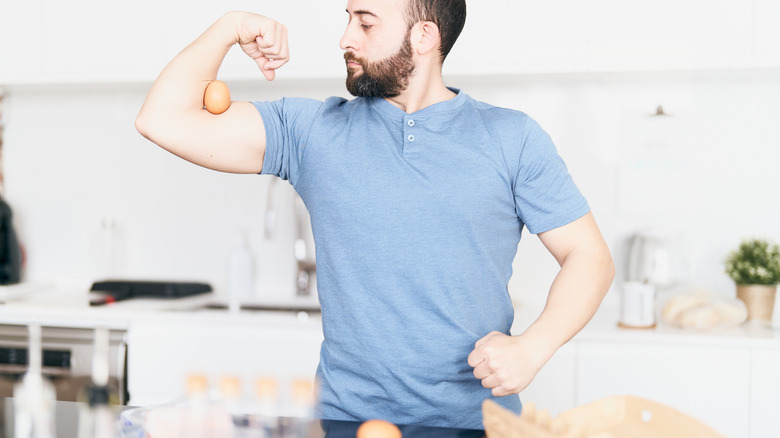 man flexing bicep and balancing egg in arm