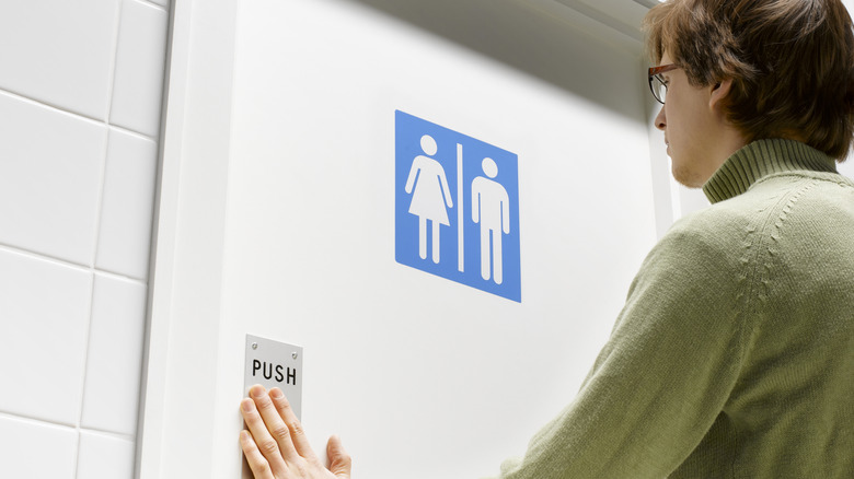 young adult pushing the door to a public restroom