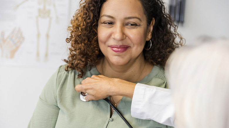 smiling woman getting heart evaluated by doctor