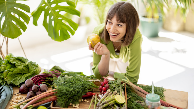 smiling woman holding pear in front of table of produce