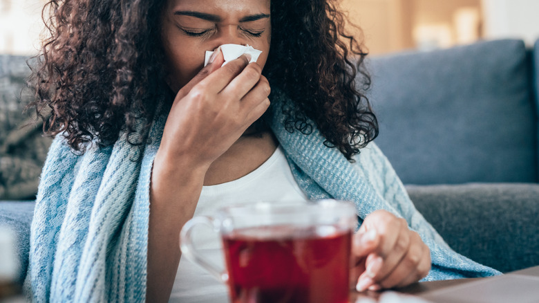 woman blowing nose with red drink in front of her