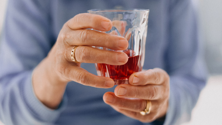 older woman with small glass of dark red beverage