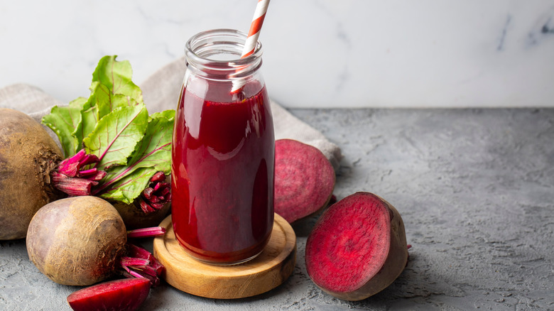 A glass of beetroot juice surrounded by beets and beet greens