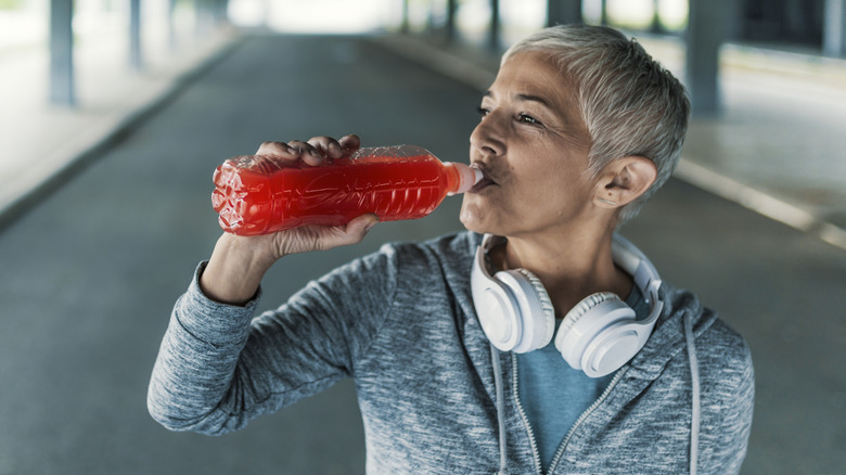 An older woman drinking red liquid from a plastic bottle