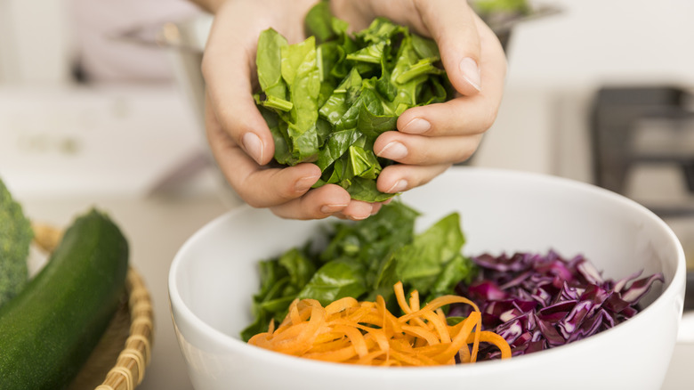 A woman's hands adding herbs to a vegetable bowl