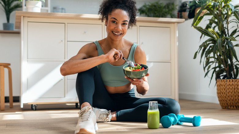 A fit woman sitting on the floor eating a bowl of fruit