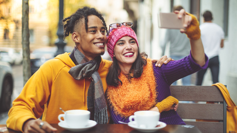 man and woman taking selfie at cafe