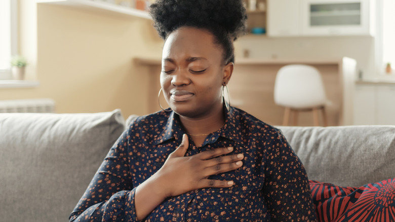 Pained woman clutching chest on sofa