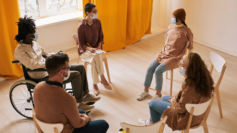 Group therapy session with 4 masked patients sitting in a circle led by a masked mental health professional