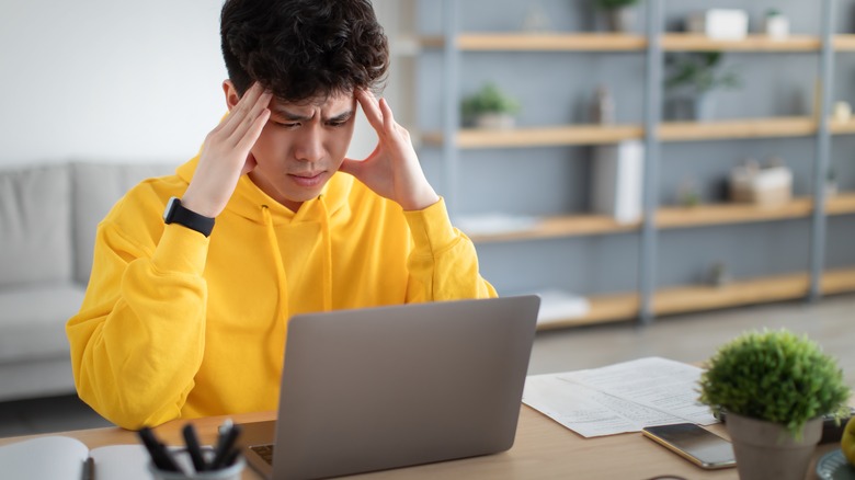 Anxious man frowns at laptop with hands at his head