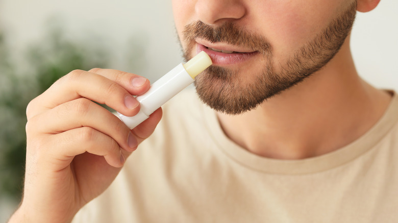 Close up of young bearded man applying stick of lip balm
