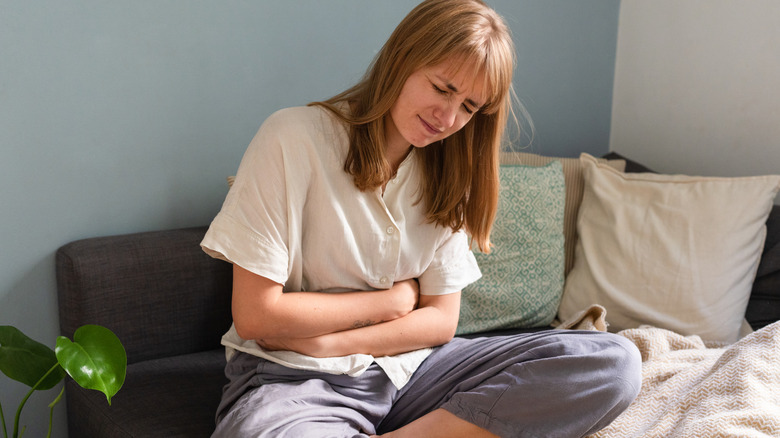 A woman sitting on her couch holding her painful stomach