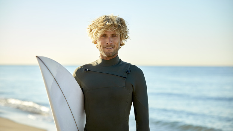 Man with blond hair carrying surf board