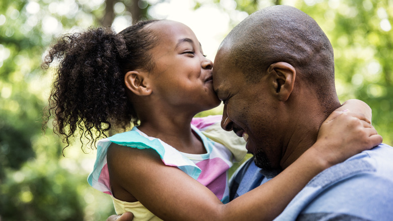 bald dad embracing daughter who's kissing his forehead