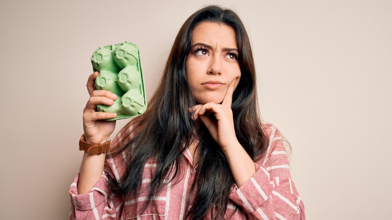 pensive-looking woman holding carton of eggs