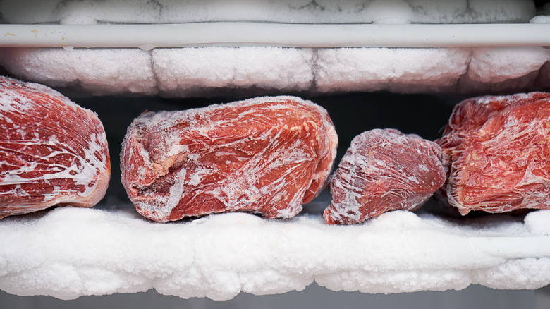 Frozen chunks of meat in a freezer surrounded by frost and ice