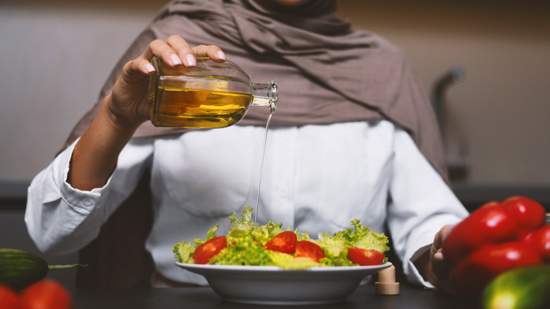Woman drizzling oil over salad