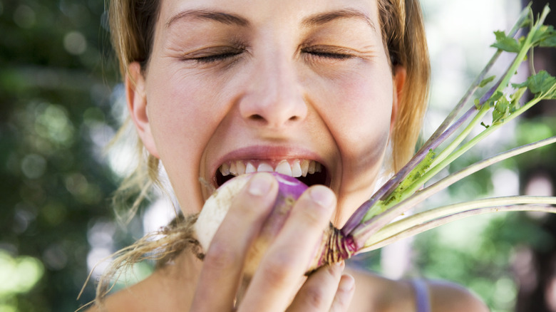 woman biting into a raw turnip outside