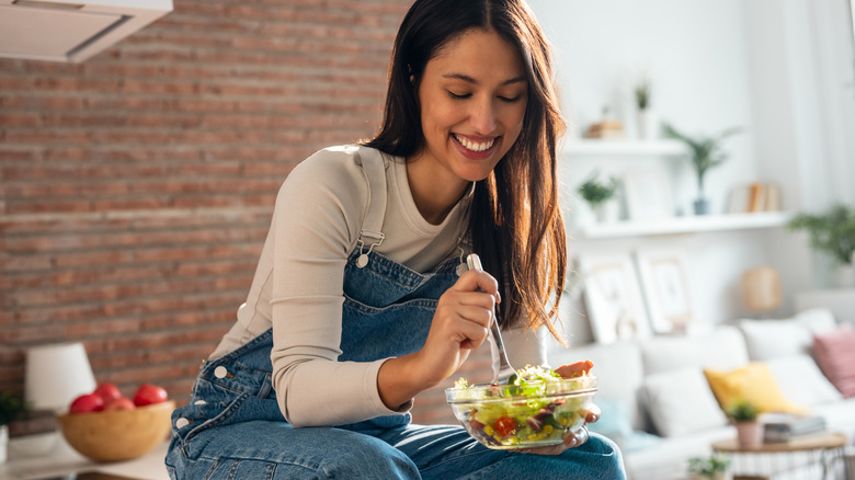 A woman sitting on her kitchen counter eating salad