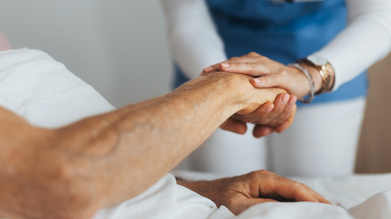 A hospital worker's hand holding a male patient's hand