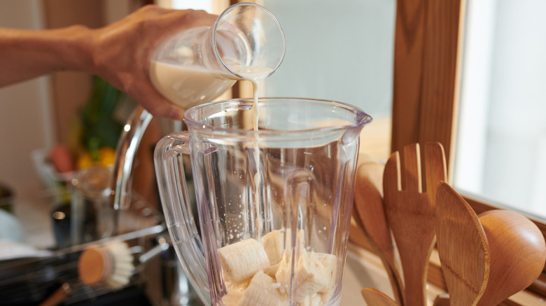 man pouring milk into banana in blender