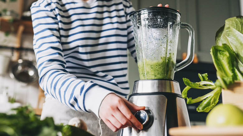 A woman's hand blending greens in a blender