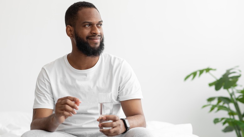Bearded man holding vitamin and water glass