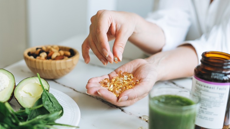 Person holds a handful of vitamin D capsules surrounded by healthy foods