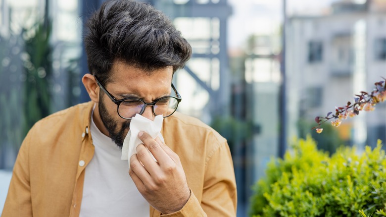 man blowing his nose outdoors