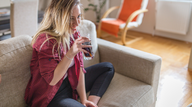 happy woman on couch drinking red juice in glass