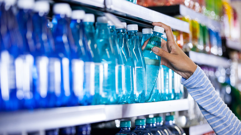 woman grabbing a bottle of water off the store shelf