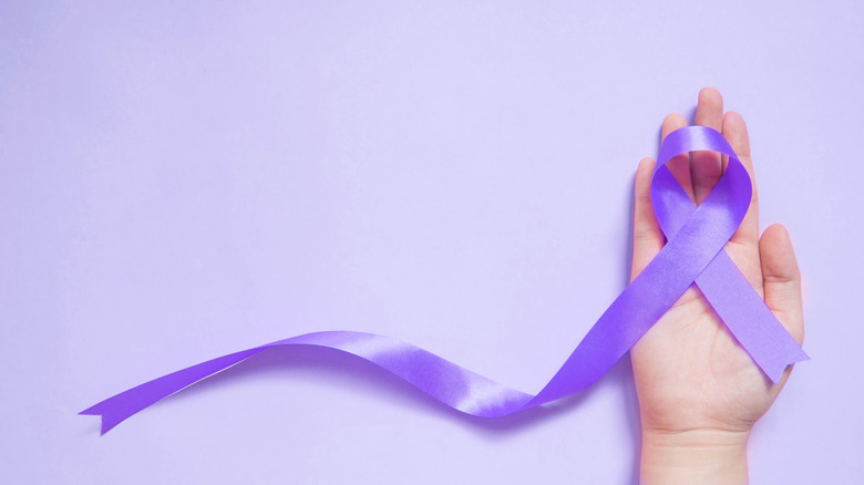 A hand holding a purple Alzheimer's ribbon with a trailing tail