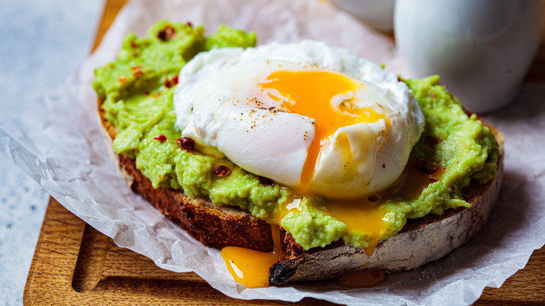 Avocado toast with a poached egg on wooden cutting board