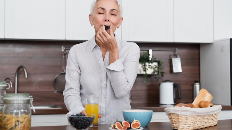 Senior woman eating figs in her kitchen