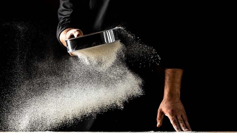 Chef sieving flour on black background