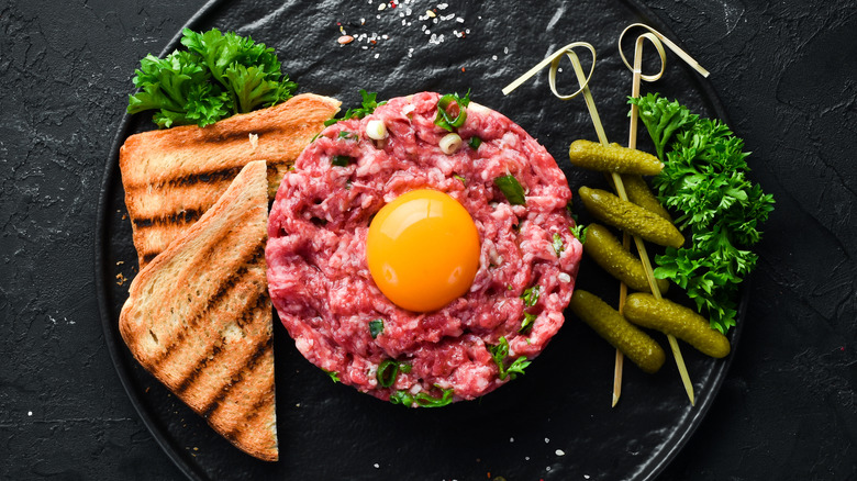 top view of steak tartar with bread and pickles