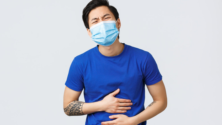 asian man wearing mask and holding tummy because of pain