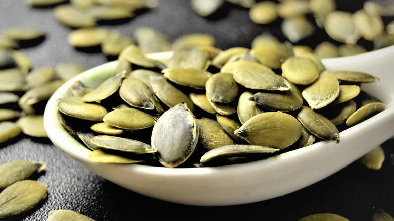 Pumpkin seeds in a spoon with other seed scattered around