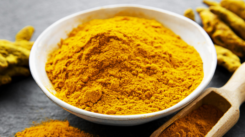 A bowl of ground turmeric with dry roots in the background