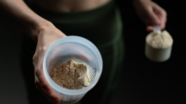 Close up of women with measuring scoop of whey protein, jar and shaker bottle, preparing protein shake.