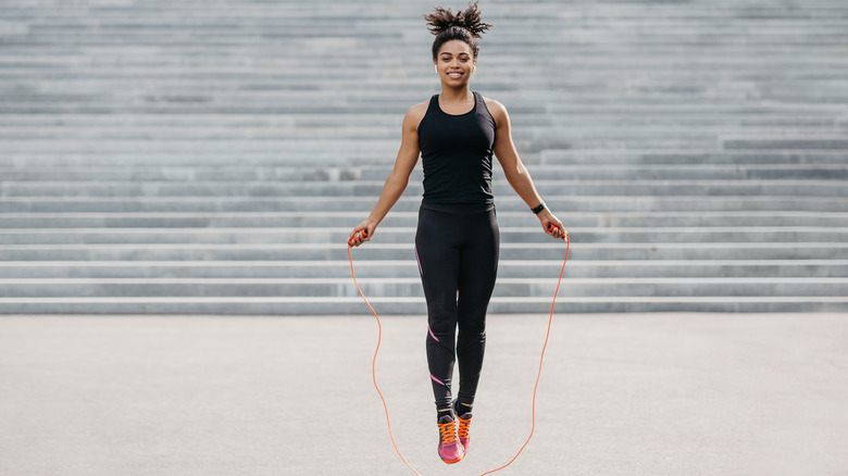 Smiling woman in black tank top and leggings jumping rope outside