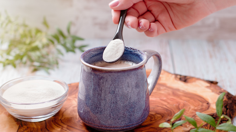 hand adding spoonful of collagen powder to coffee