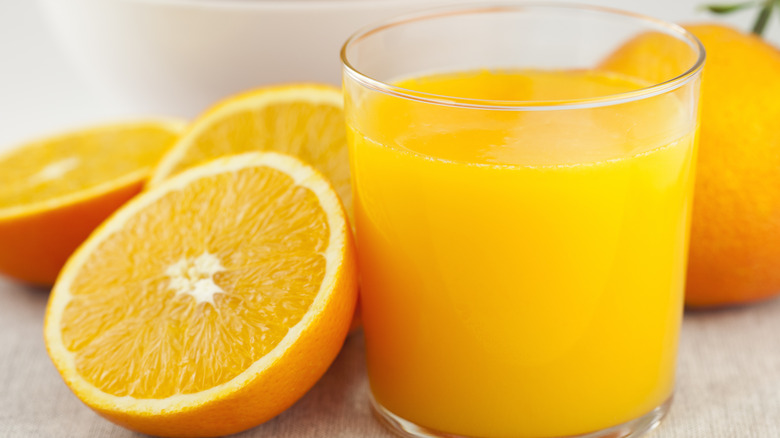 Glass of orange juice next to sliced oranges