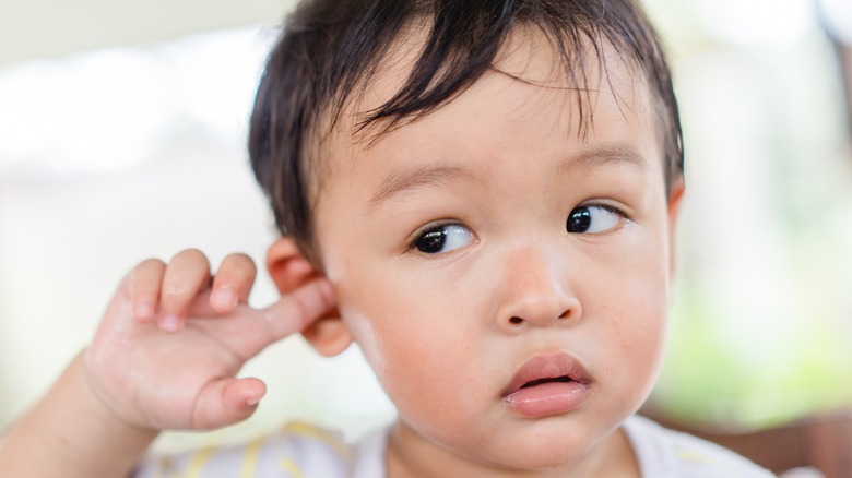 Male toddler sticking finger in ear