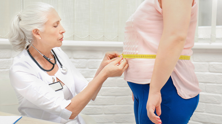 doctor measuring older woman's waist