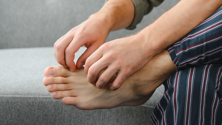 man scratches foot with two hands
